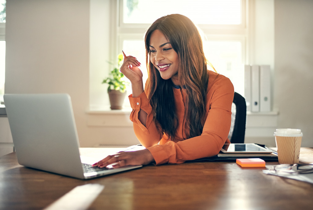 Smiling young African female entrepreneur sitting at a table in her home office working on a laptop