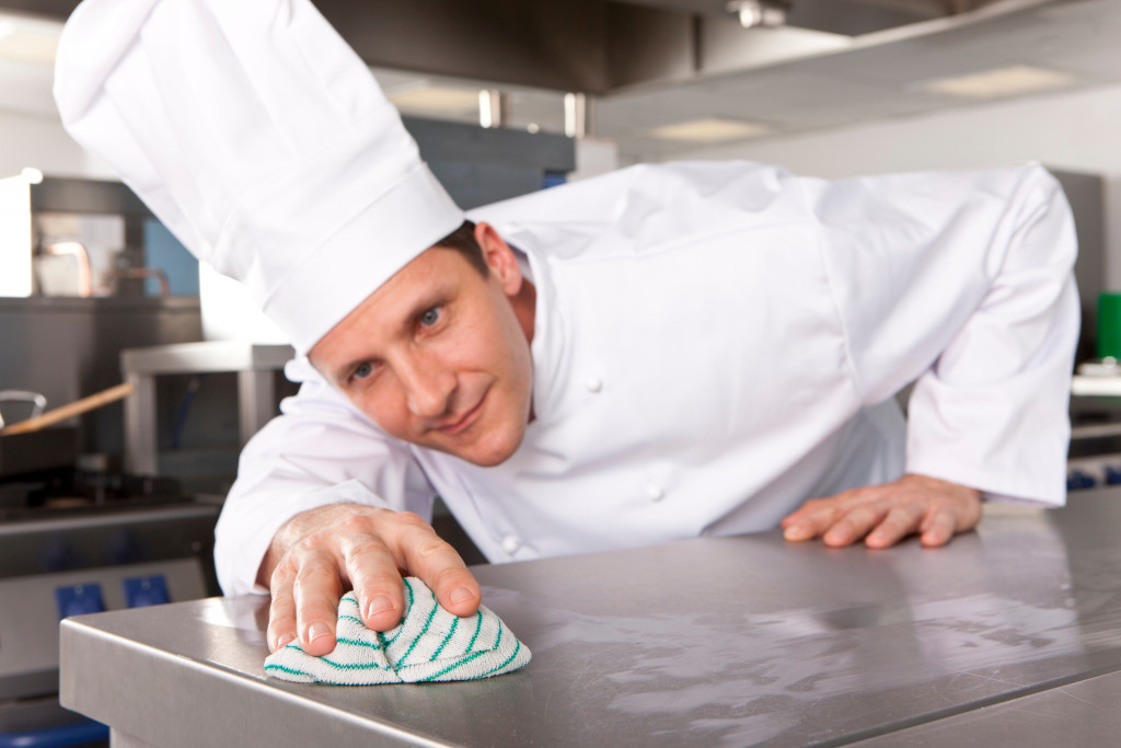 a man in a chef uniform wiping stainless teel counter