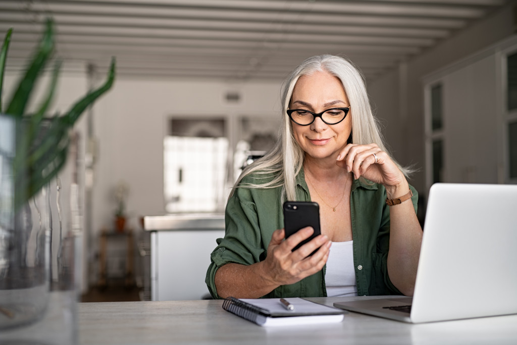 Smiling cool old woman wearing eyeglasses messaging with smartphone