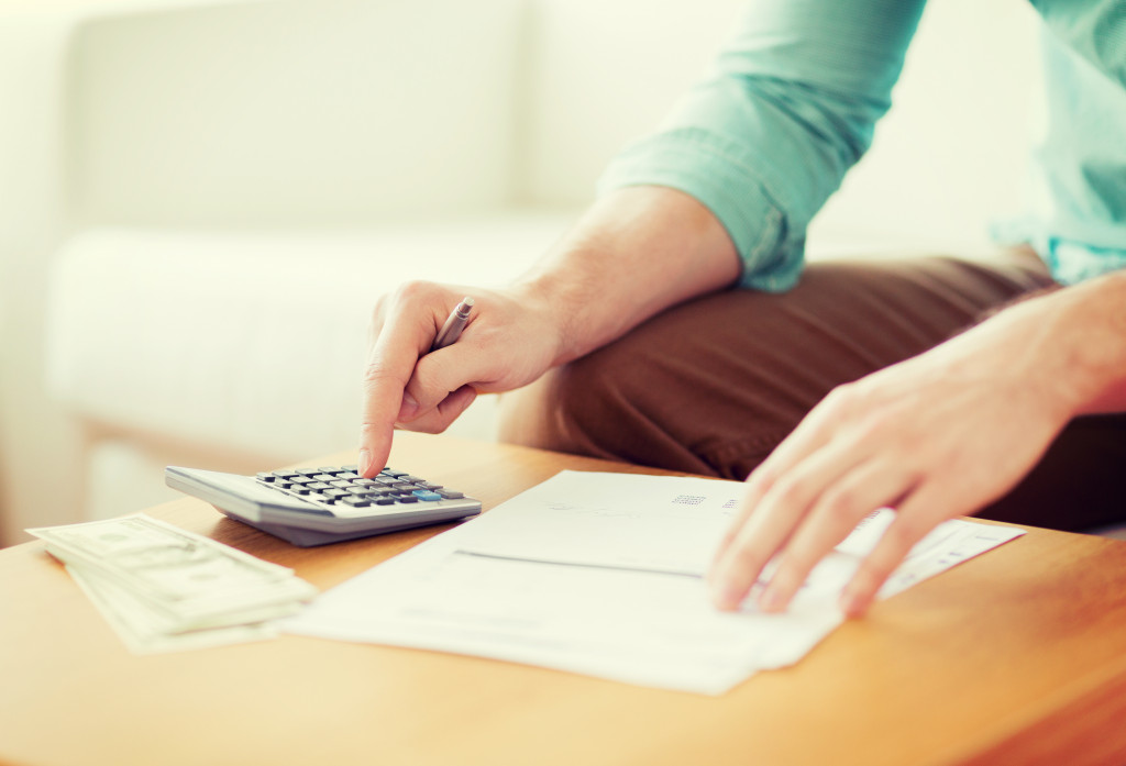 close up of man with calculator counting money and making notes at home