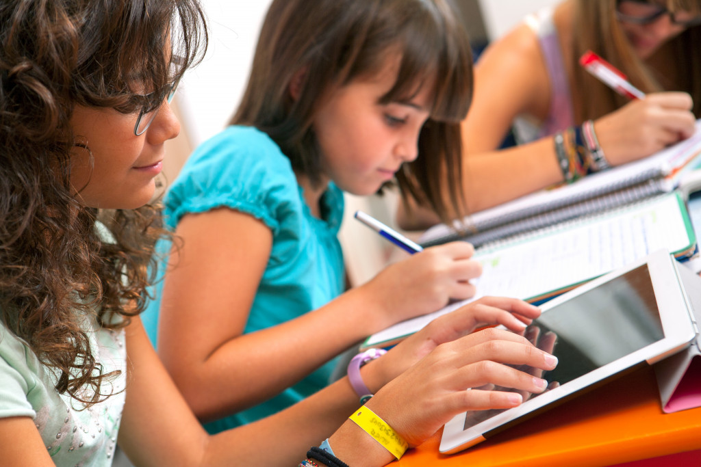 A student writing notes while other is using a tablet for taking notes